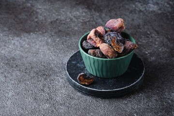 Dried dark figs in a green bowl on a green concrete background. Dried fruits. Ingredients for cooking.