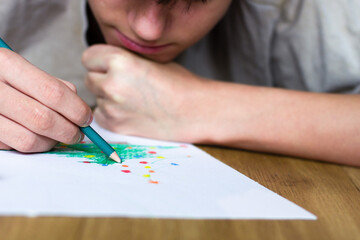 A teenage boy lying on the floor draws a Christmas tree with colored pencils ©  Mila Lazo