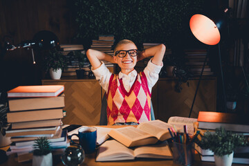 Young student wearing stylish argyle vest and glasses enjoys a study session at home, surrounded by...