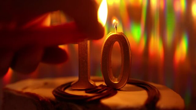 A cake with a golden candle with the number 10. On a holographic background, with shimmering movements. The candle flame is sparkling. High quality 4k footage