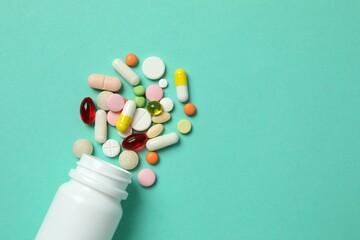 Various pills pouring out of medicine bottle on color background