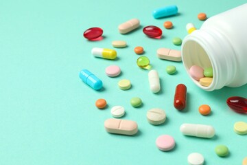 Various pills pouring out of medicine bottle on color background