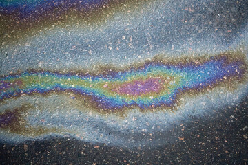 Colorful gasoline or oil spill creates a rainbow sheen on asphalt road surface, indicating pollution and environmental damage