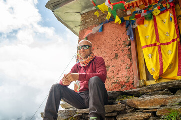 Smiling Backpacker sitting on small sacred Buddhist monastery doorstep decorated multicolored...