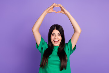 Joyful woman with long brunette hair making heart shape with hands on a vibrant purple background