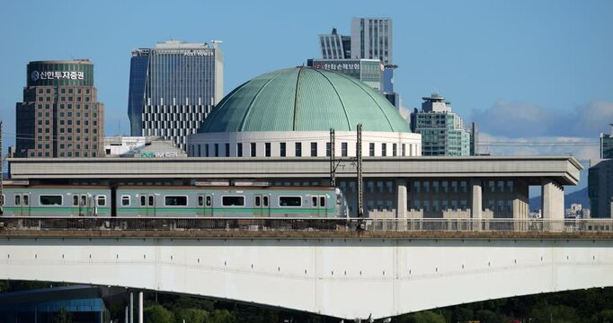 Line 2 metro train rides on viaduct bridge, National Assembly building of South Korea seen in background.
