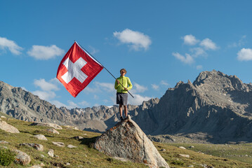 Obraz premium Hiker Man waving an Switzerland flag. The tourist reached the summit.