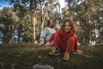 Fototapeta premium A young girl is sitting on a rock in a forest with her mother