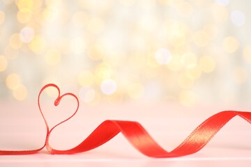 Heart made of red ribbon on table against blurred lights, space for text. St. Valentine's day card