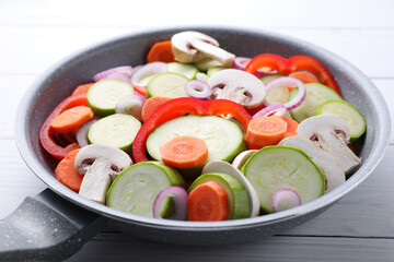 Frying pan with mix of fresh vegetables and mushrooms on white wooden table, closeup