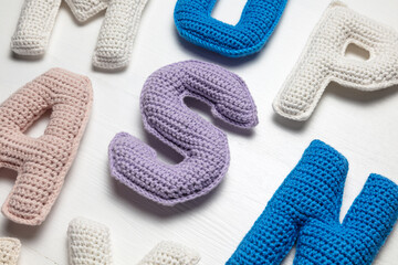 Handmade crocheted alphabet letters on a white background, showcasing colorful designs with blue, purple, pink, and white yarn.