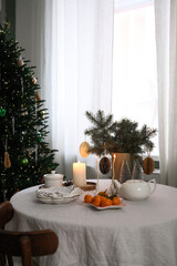 A beautifully warm and inviting Christmas holiday table decor with plates, candles, vase with spruces branches, teapot, mandarins.