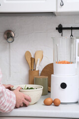 A beautifully stylish kitchen scene showcases a modern blender surrounded by vibrant fresh vegetables and eggs, woman hands with green leaves.