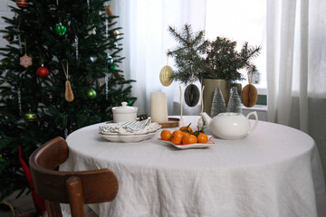 A beautifully warm and inviting Christmas holiday table decor with plates, candles, vase with spruces branches, teapot, mandarins.