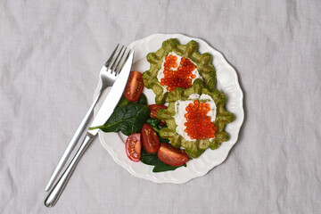 Spinach and orange lentils vafles with cottage cheese, caviar garnished with Tomato and Spinach, beautifully presented on white plate. Top view.