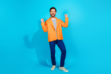 Cheerful young man in an orange jacket stands happily against a bright turquoise background