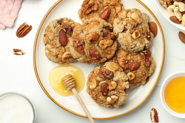 Tasty cookies with nuts, honey dipper and milk on white table, flat lay