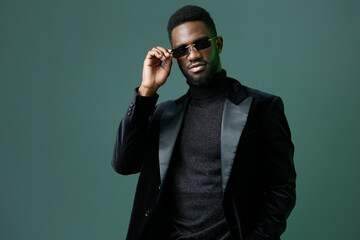 Fototapeta premium Confident black man in suit and sunglasses standing against green background, exuding professionalism and style