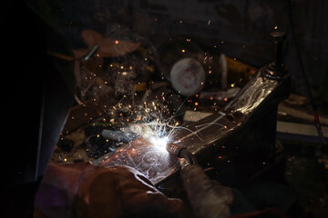 Welding old metal car part at workshop, sparks and smoke flying around, closeup detail