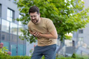 A young man does sports and runs on the street, stands bent over and holds his hands to his chest,...