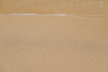 Sandy beach, lit by sun, sea water washes over, closeup detail - abstract shallow depth of field tropical vacation background