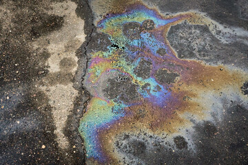 A shimmering gasoline spill creates a vibrant rainbow on asphalt, raising awareness of...