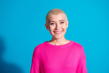 Young woman with a bright smile wearing a pink pullover stands confidently against a vibrant blue...