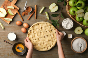 Woman making homemade apple pie and ingredients on wooden table, top view