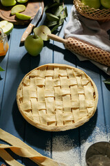 Uncooked homemade apple pie and ingredients on blue wooden table