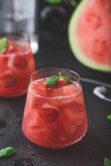 Glass of watermelon and strawberry cocktail with mint garnish on dark concrete background
