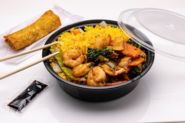 Chinese restaurant food to go. Shrimp with veggies in garlic sauce served with fried rice. Chopsticks, soy sauce packet and spring roll on the side.