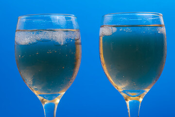 Two Glasses of Sparkling Beverage with Ice Against a Vibrant Blue Background
