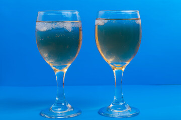 Close-up of two glasses of white wine with ice on a vibrant blue background