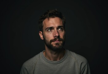 Fototapeta premium A pensive man with a beard, gazing thoughtfully into the distance against a dark background.