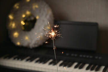 Christmas and New Year celebration. Sparkler in woman hand, piano with wreath on the background