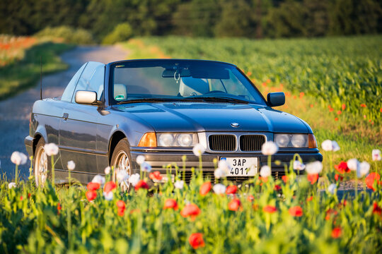 Prague, Czech republic - June 10, 2024. Grey convertible BMW E36 parked on the road by poppy field