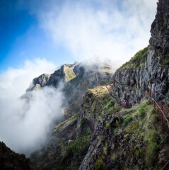 A dramatic view of Vereda Pico do Arieiro, Madeira, Portugal. A narrow mountain trail winds along rugged cliffs surrounded by dense clouds, offering a surreal and adventurous atmosphere.