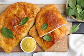 Tasty calzones with basil, cheese and sauce on table, top view