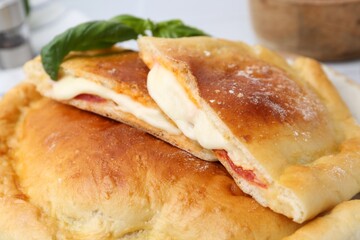 Pieces of delicious calzone pizza with mozzarella, tomatoes and basil on table, closeup