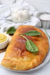 Tasty calzone with basil and sauce on white table, closeup