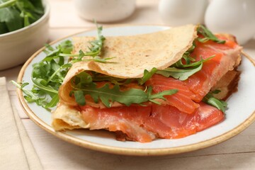 Delicious crepes with salmon and arugula on white wooden table, closeup