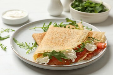 Delicious crepes with salmon, cream cheese and arugula on white table, closeup