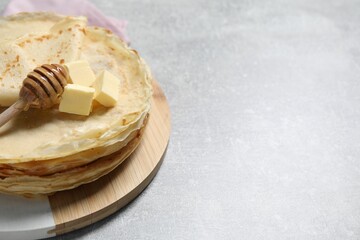 Tasty crepes with butter and honey on grey textured table, closeup. Space for text