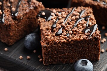 Delicious chocolate puffed rice bars and blueberries on black wooden board, closeup