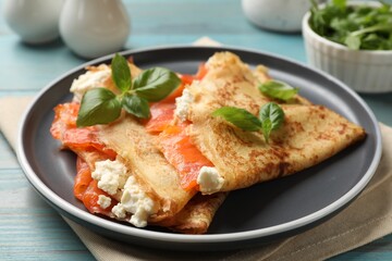 Delicious crepes with salmon, cream cheese and basil on light blue wooden table, closeup