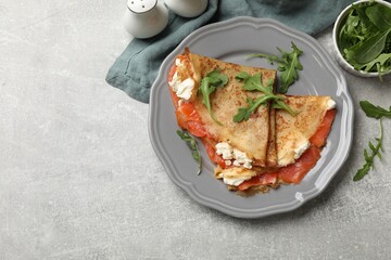 Delicious crepes with salmon, cream cheese and arugula on grey table, flat lay. Space for text