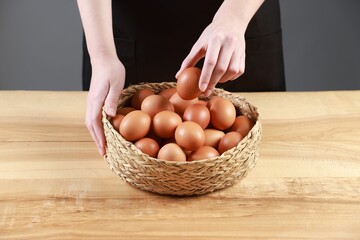 Woman with basket of eggs at wooden table on grey background, closeup