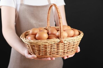 Woman with basket of eggs on black background, closeup