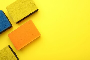 Many color sponges on yellow background, flat lay. Space for text