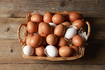 Many raw eggs in basket on wooden table, above view